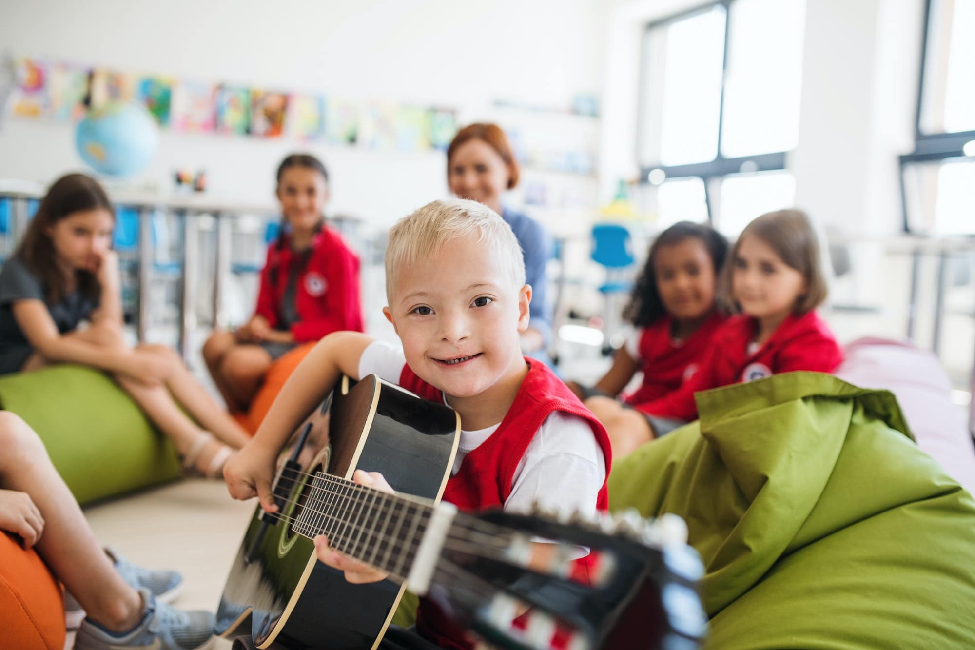 A down-syndrome boy with school kids and teacher sitting in class, playing guitar