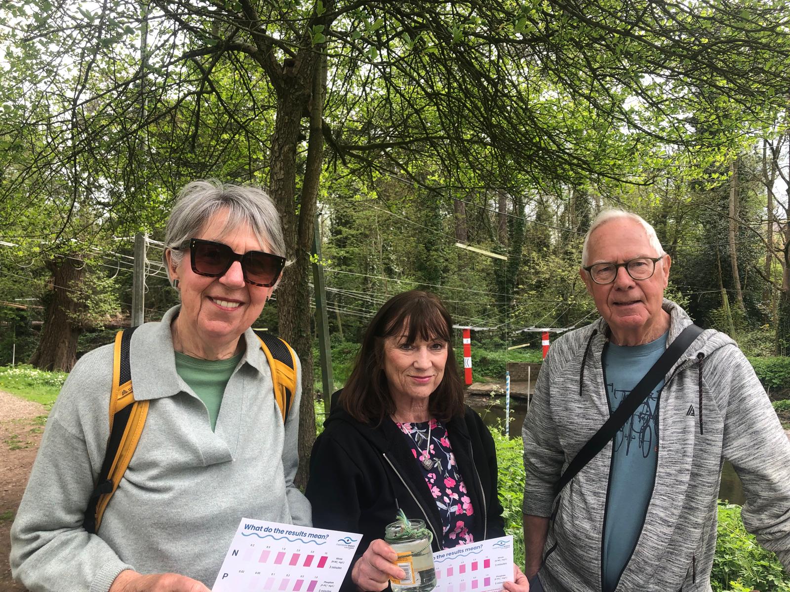 Three volunteers from Stone River Pollution Action Group standing by the River Trent holding water quality test results during the GreatWaterBlitz weekend.