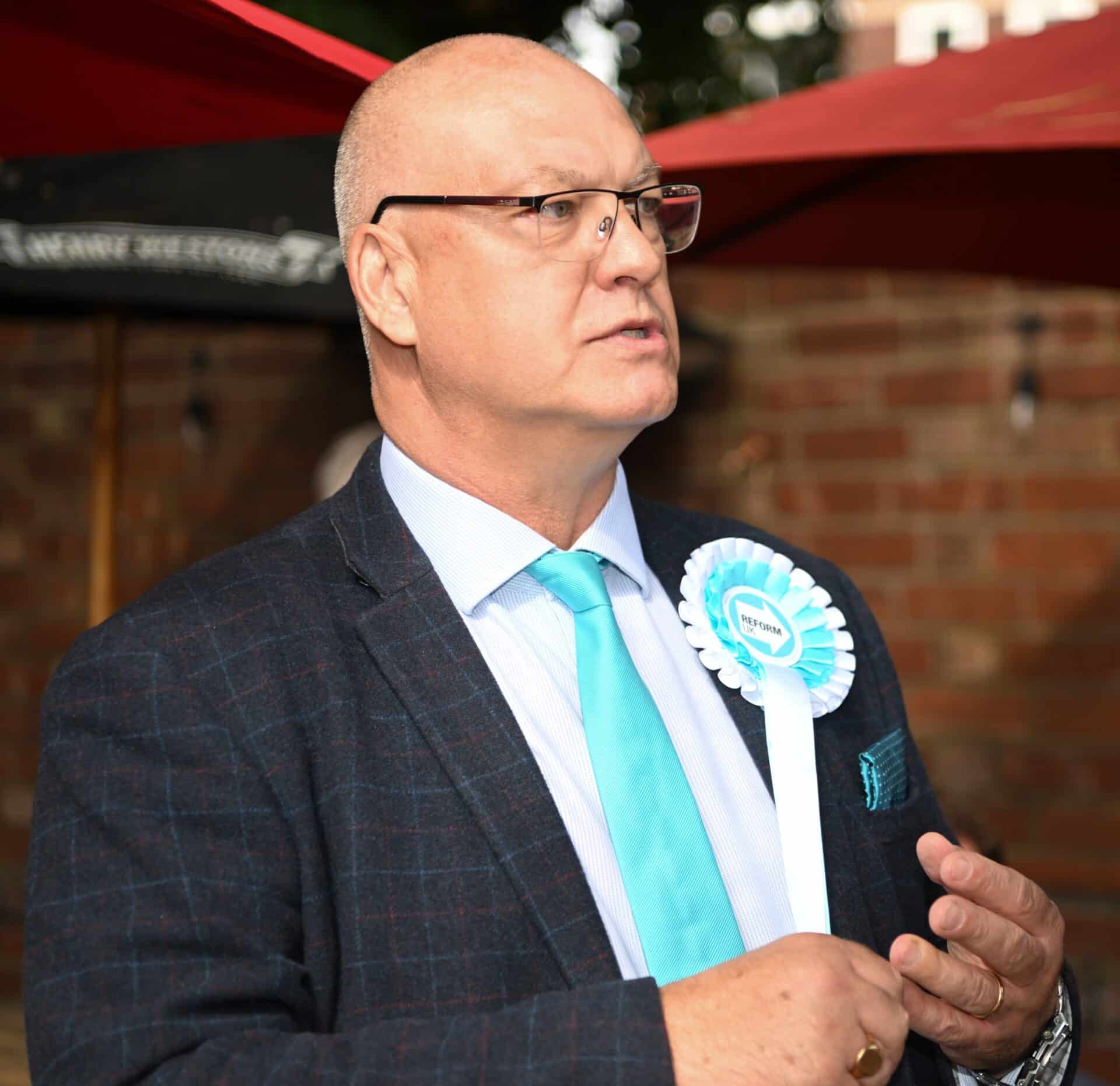Reform UK Councillor Ian Cooper in a park grey jacket, white shirt and pale blue tie and Reform UK rosette.