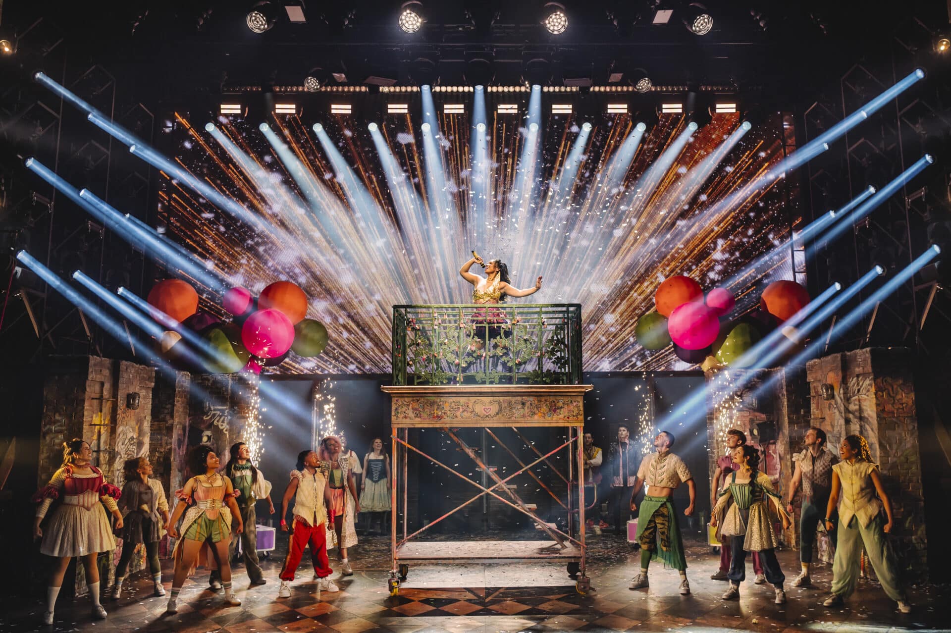 Juliet sings from a balcony as confetti bursts and beams of light shoot across the stage with the full cast gathered below during the spectacular finale of & Juliet