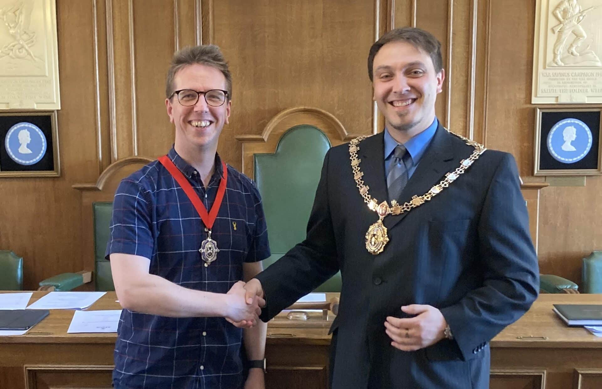 Deputy Mayor Andrew Best and Mayor Jason Metters smiling and shaking hands inside the Stone Town Council chamber.