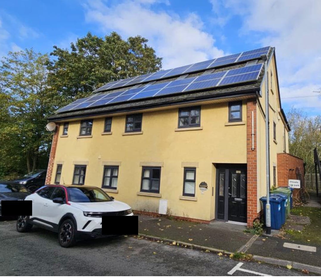 A two-storey cream and red brick building with a pitched roof covered in solar panels, identified as Sherwood House on Church Street in Stone. A white car is parked outside, and blue wheelie bins are visible near the entrance. Trees and a supermarket car park can be seen in the background.