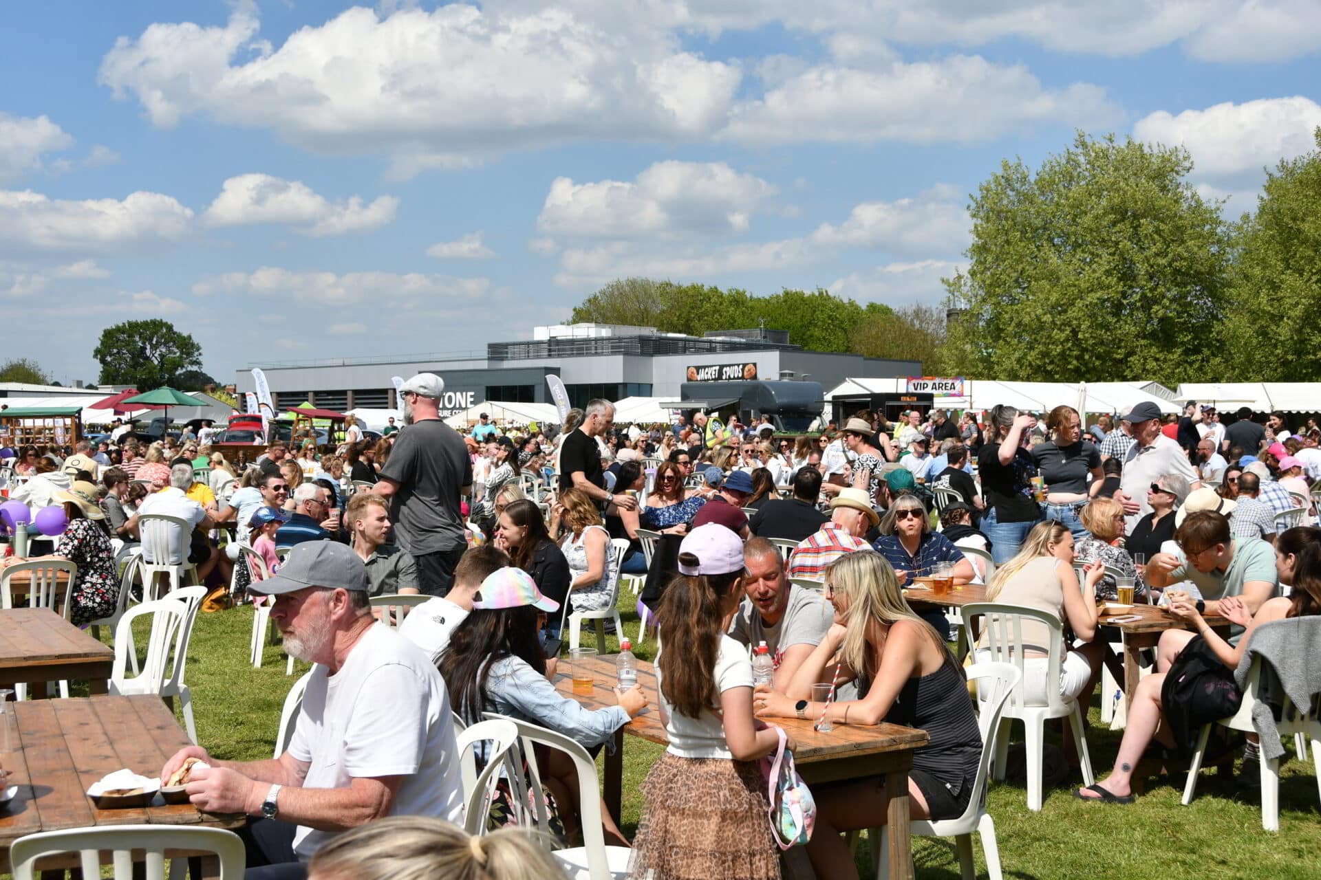 Large crowds relax and enjoy food at outdoor tables under blue skies at Westbridge Park during Stone Food & Drink Festival 2025.
