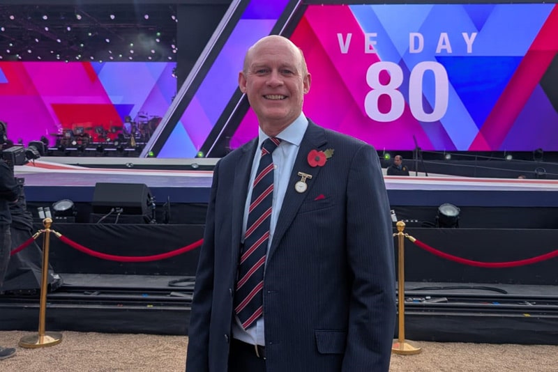 Robin McMahon smiling in front of the VE Day 80 concert stage at Horse Guards Parade in London.