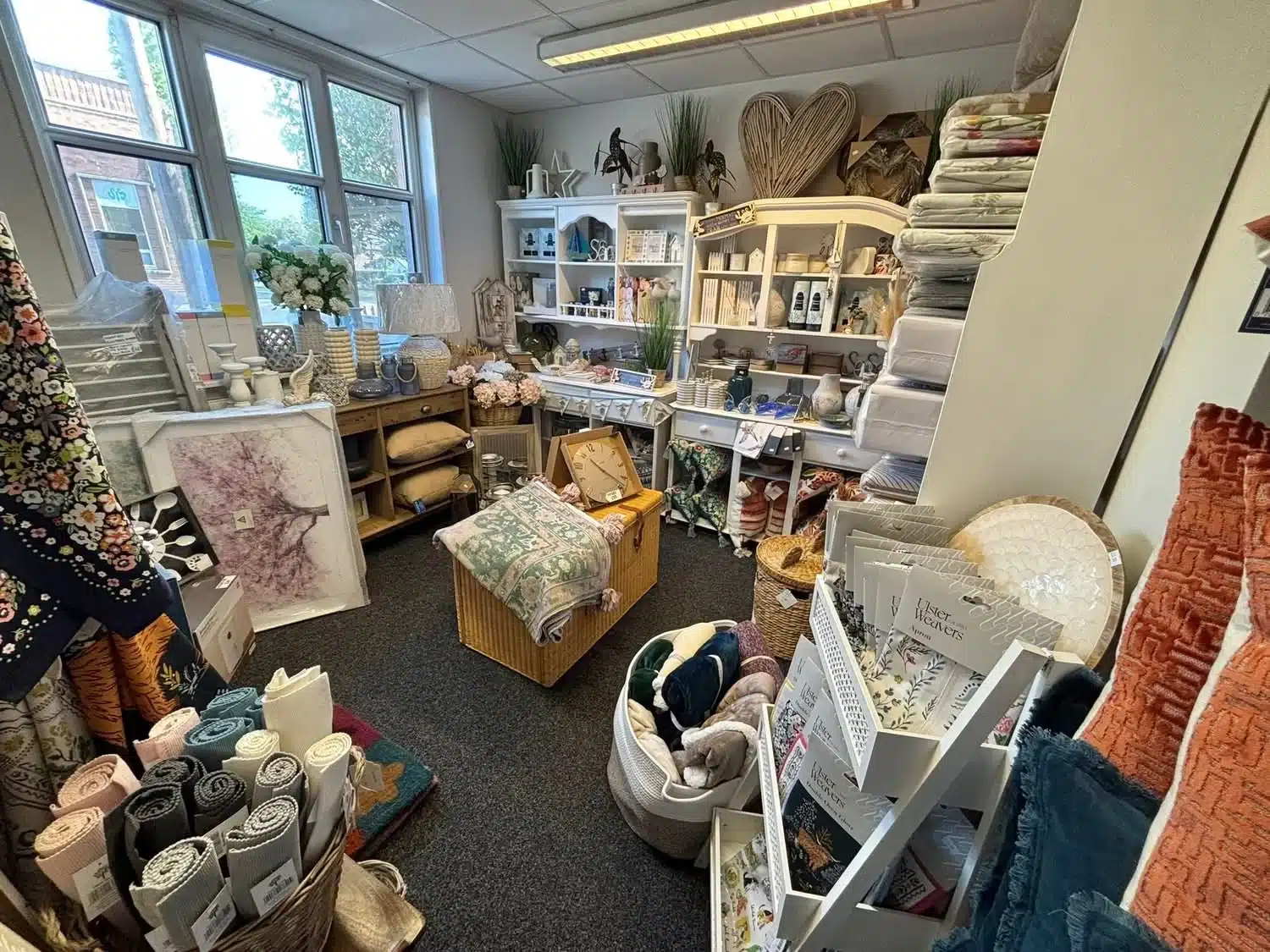 Cosy corner inside LCT Homewares with prints, kitchenware, floor mats and neatly folded blankets and cushions.