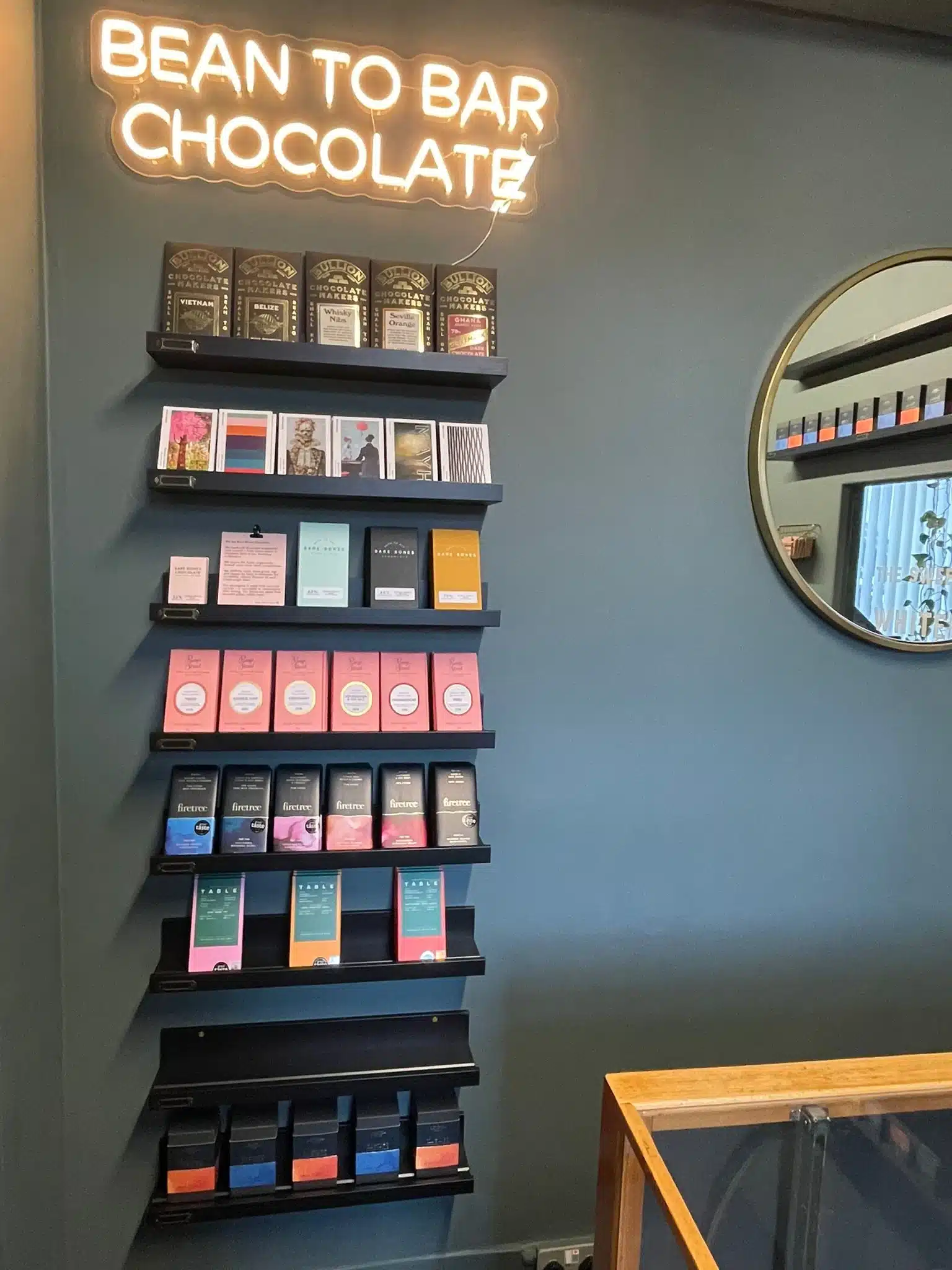 A colourful wall display of artisan chocolate bars beneath a glowing neon sign that reads “Bean to Bar Chocolate” inside The Sweet Shop of Whitebridge.