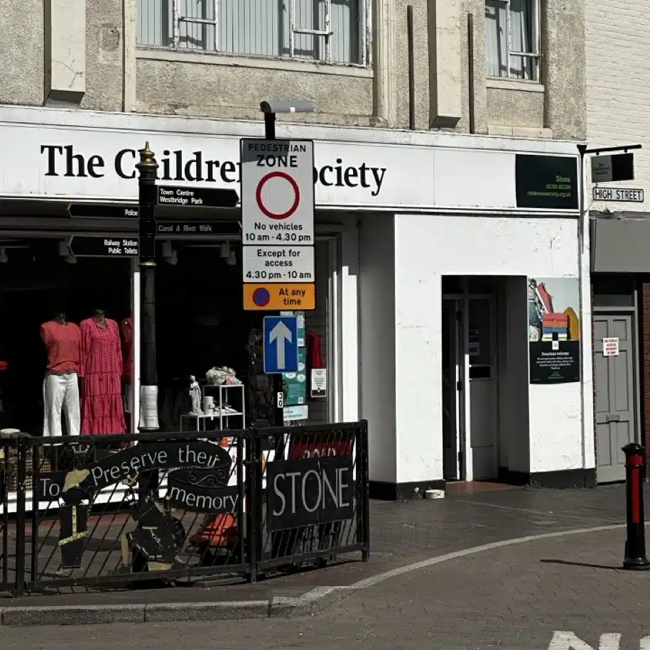 Close-up view of pedestrian zone signage on Stone High Street outside The Children’s Society, showing vehicle restriction times and access conditions.