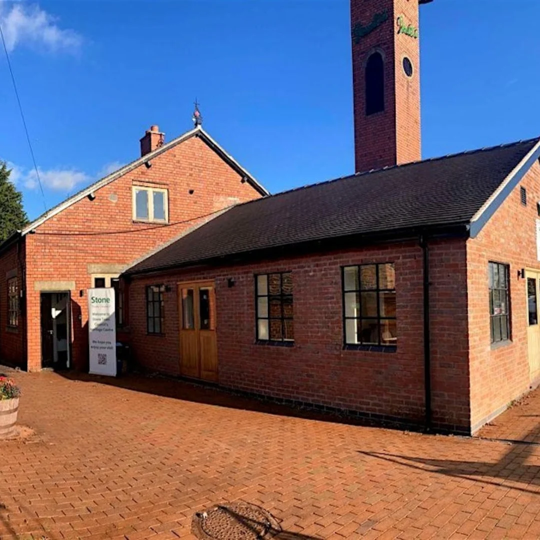 The exterior of Stone Heritage Centre on a sunny day, showing the red brick building with its distinctive chimney and a sign by the entrance.