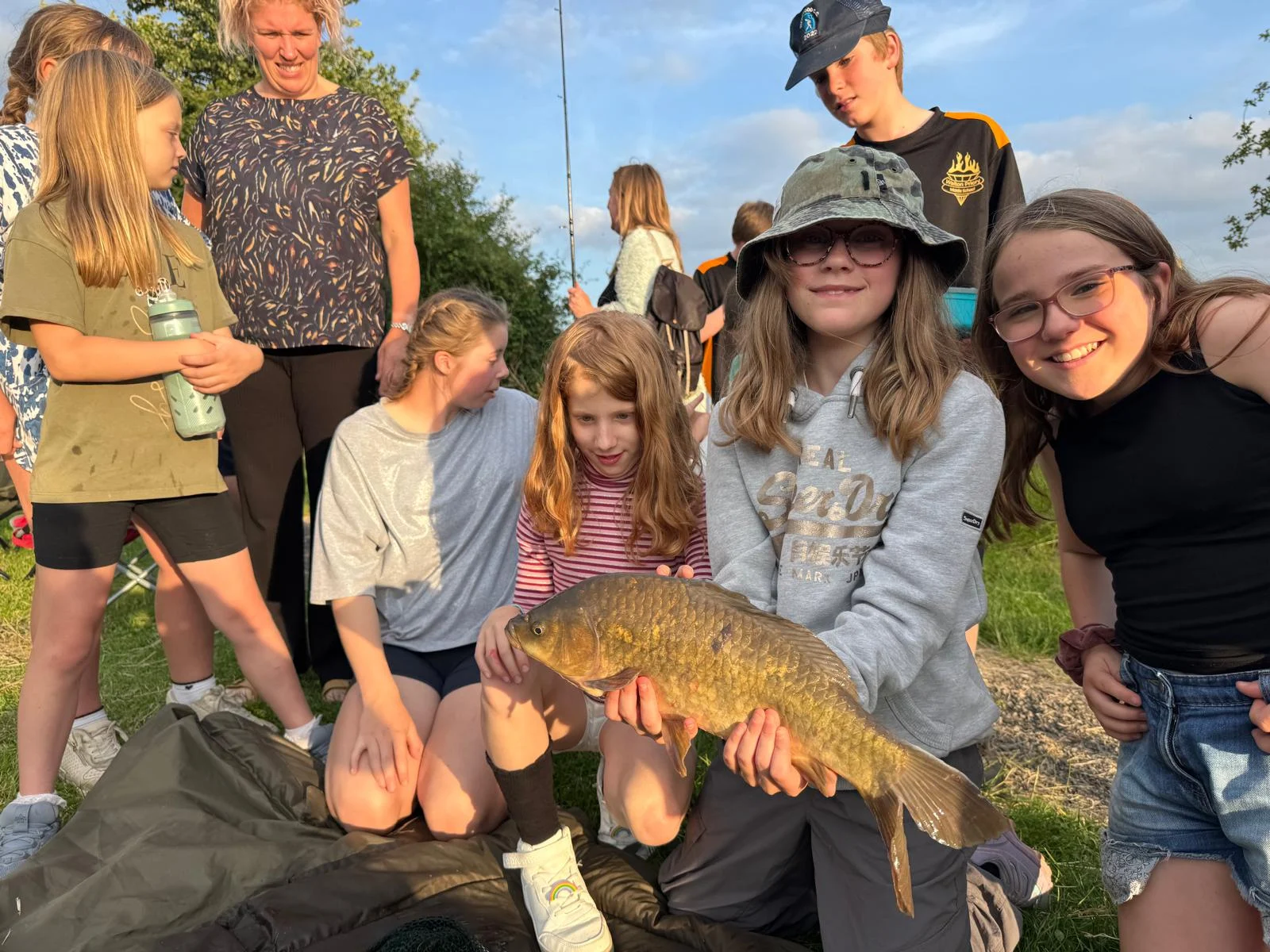 Group of young people at Crossroads Youth Club with a girl holding a freshly caught fish during an outdoor trip.