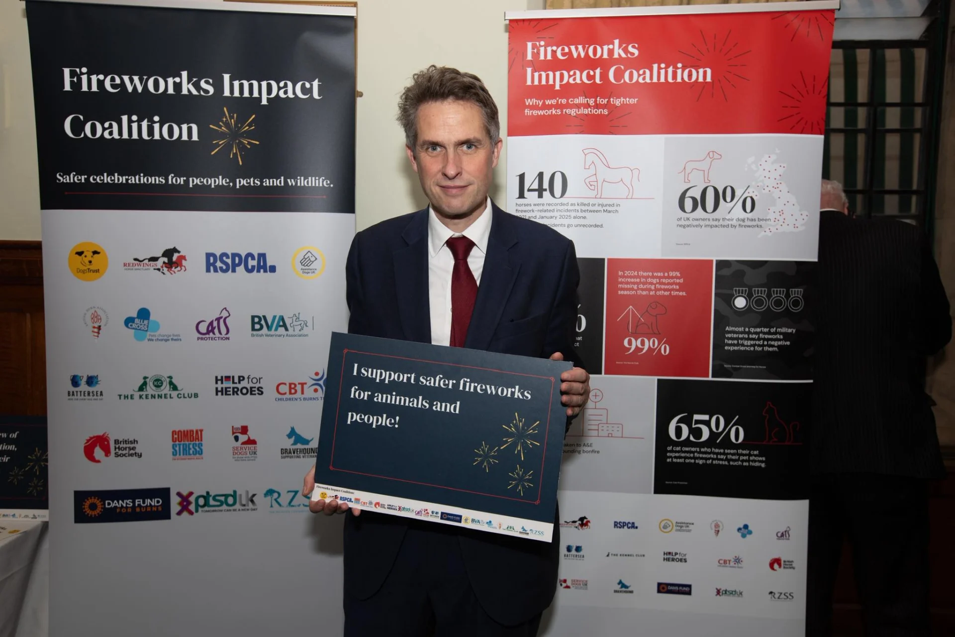 Stone MP Sir Gavin Williamson holding a sign in front of Fireworks Impact Coalition banners at a Westminster event