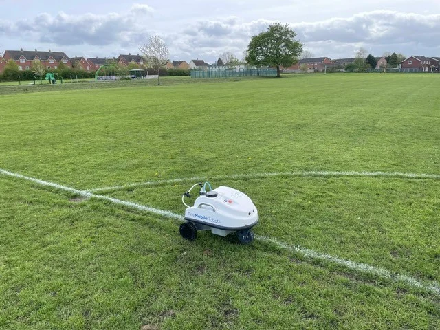A white robotic football pitch line marking machine on a grass pitch in Stafford Borough.