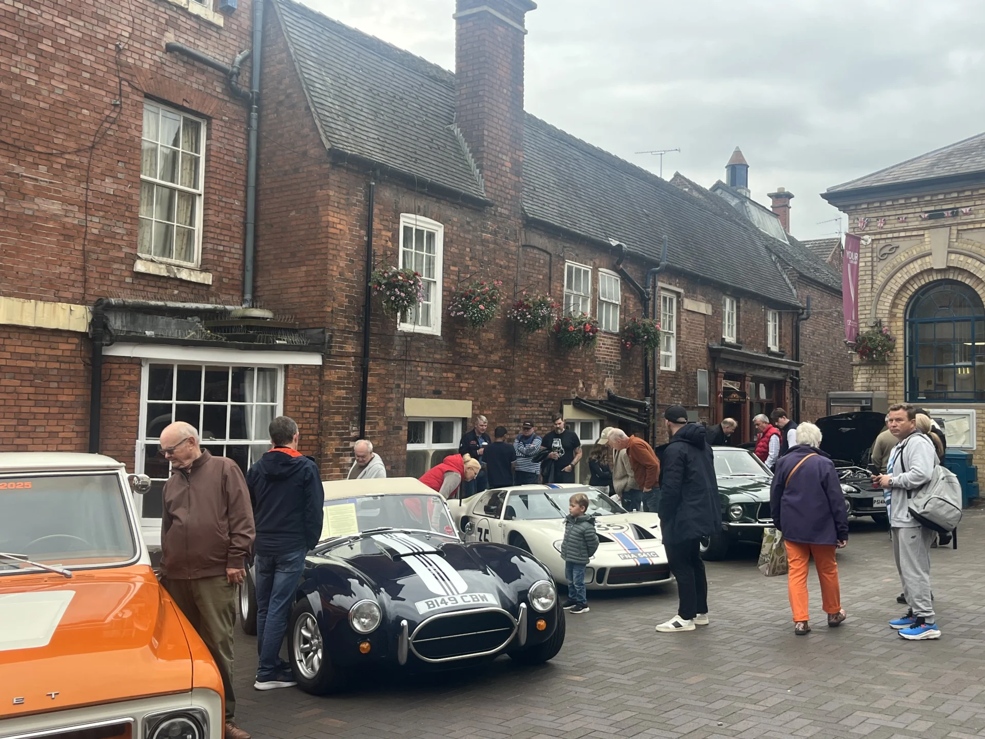 Classic cars on display in Stone Market Square, with visitors looking at vehicles including a black sports car and a white racing car.
