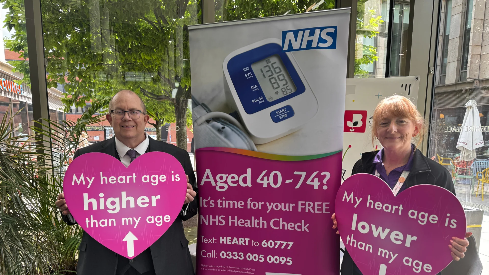 Martin Rogerson and an Everyone Health Staffordshire representative hold heart age signs beside an NHS Health Check banner.