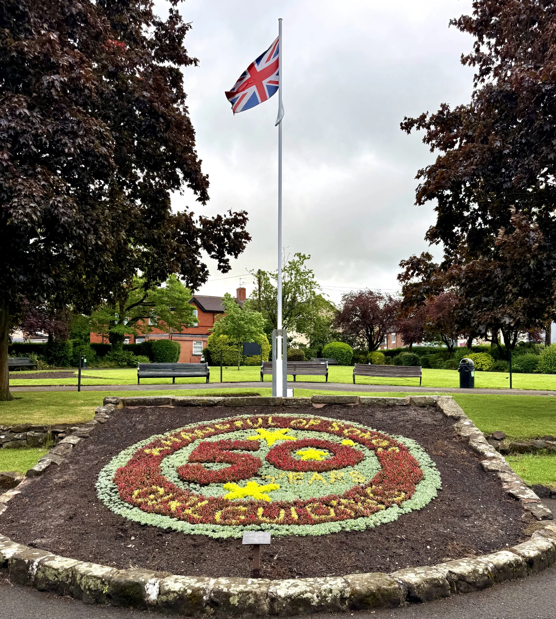 Floral carpet bed in Stonefield Park, Stone, marking 50 years of Girlguiding’s A Handful of Songs, with a Union flag above.