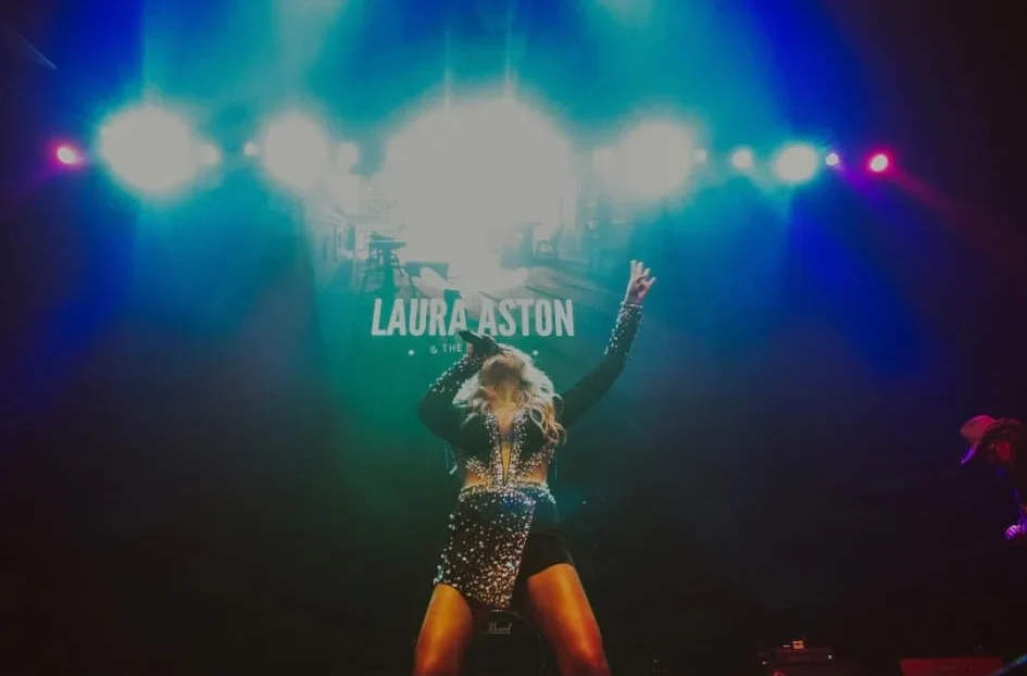 Laura Aston performing on stage under bright lights.