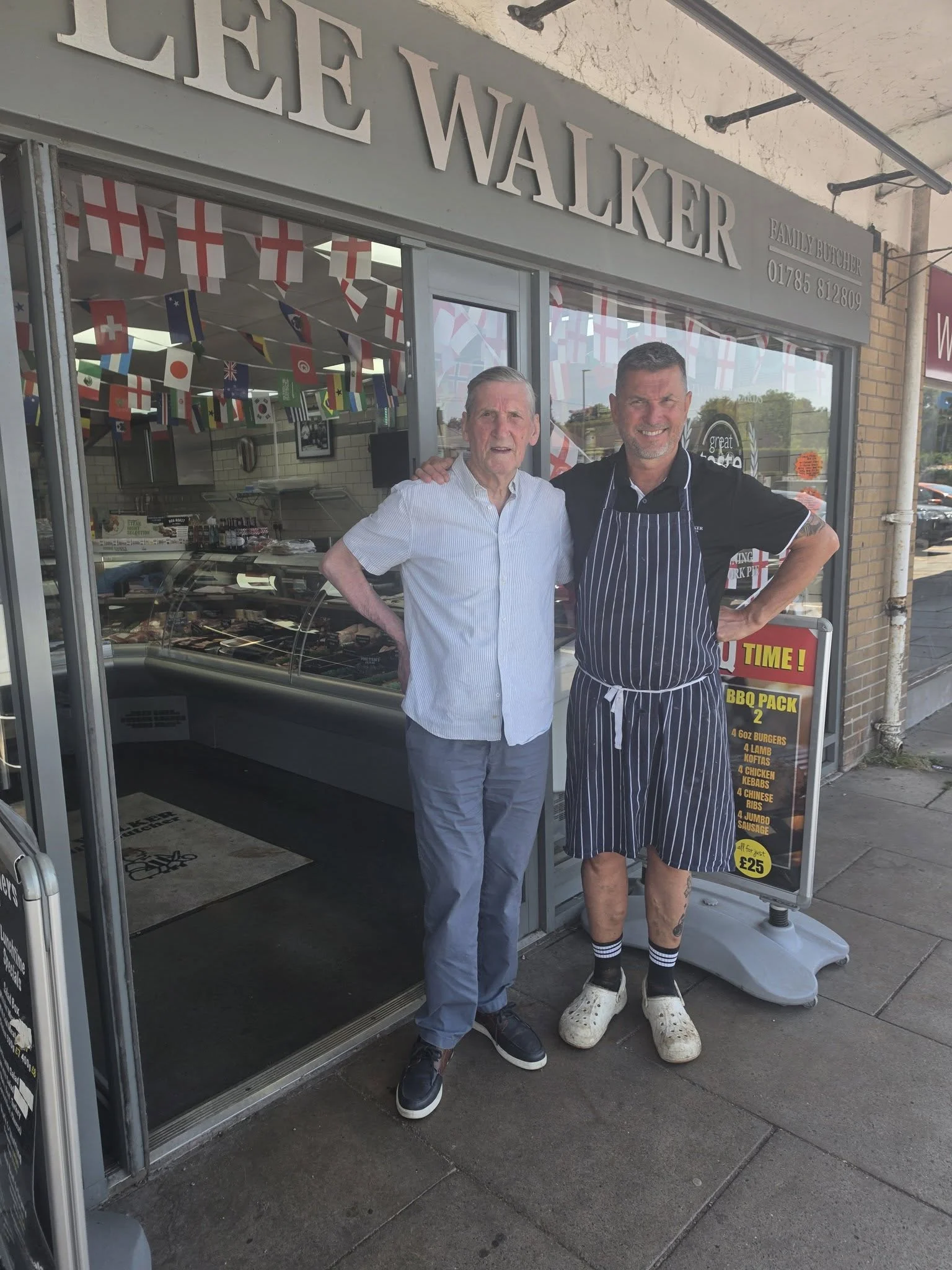 Two men standing outside Lee Walker Butchers in Stone, with the shopfront and meat counter visible behind them.