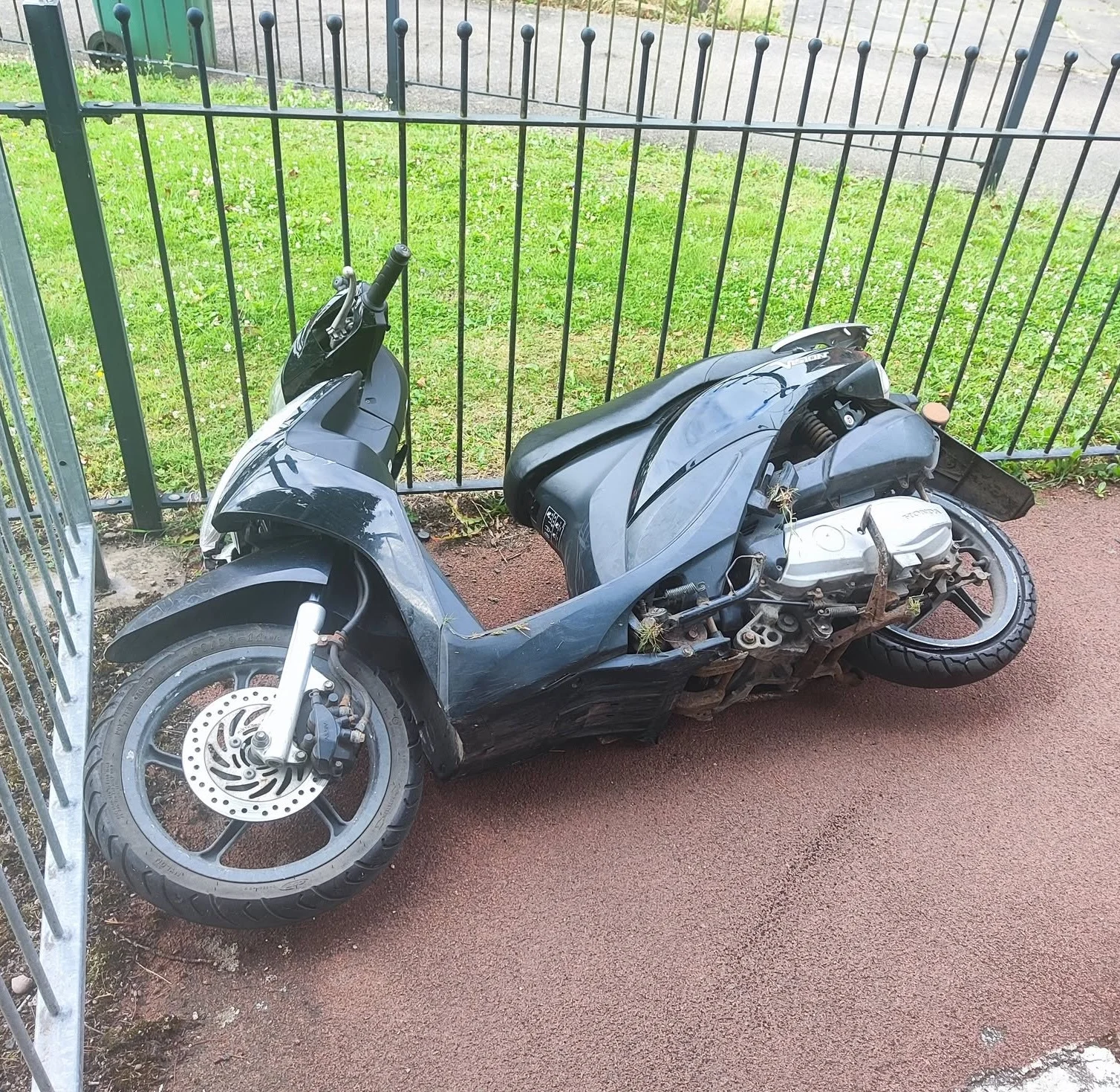A black moped lying on a footpath beside railings.