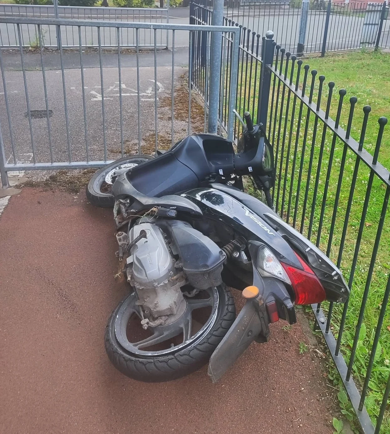 A black moped lying on a footpath beside railings.