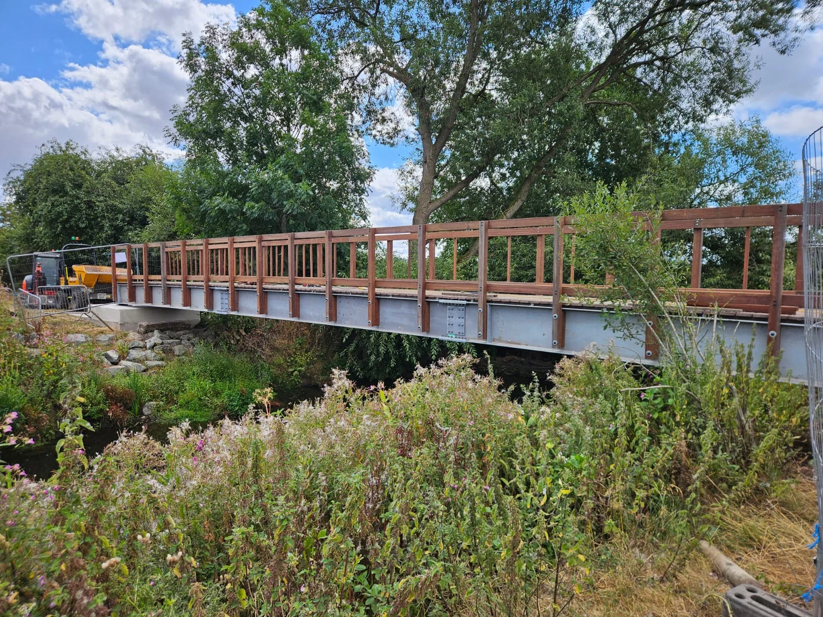 New footbridge spanning the river on Sandon and Burston Public Footpath 36, with construction equipment visible nearby.