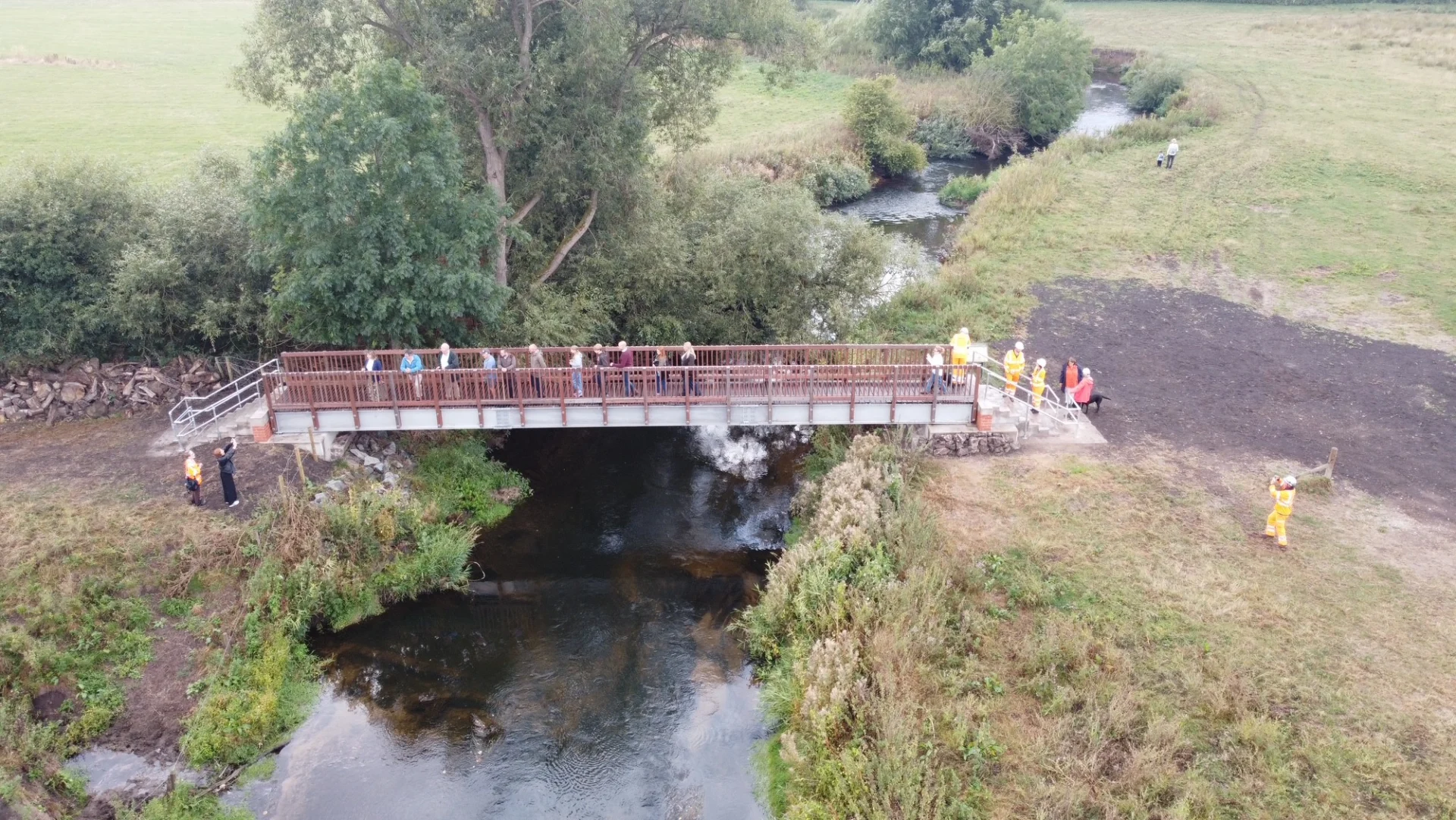 Aerial view of the new Burston footbridge crossing the River Trent, with walkers on the bridge and council staff nearby.