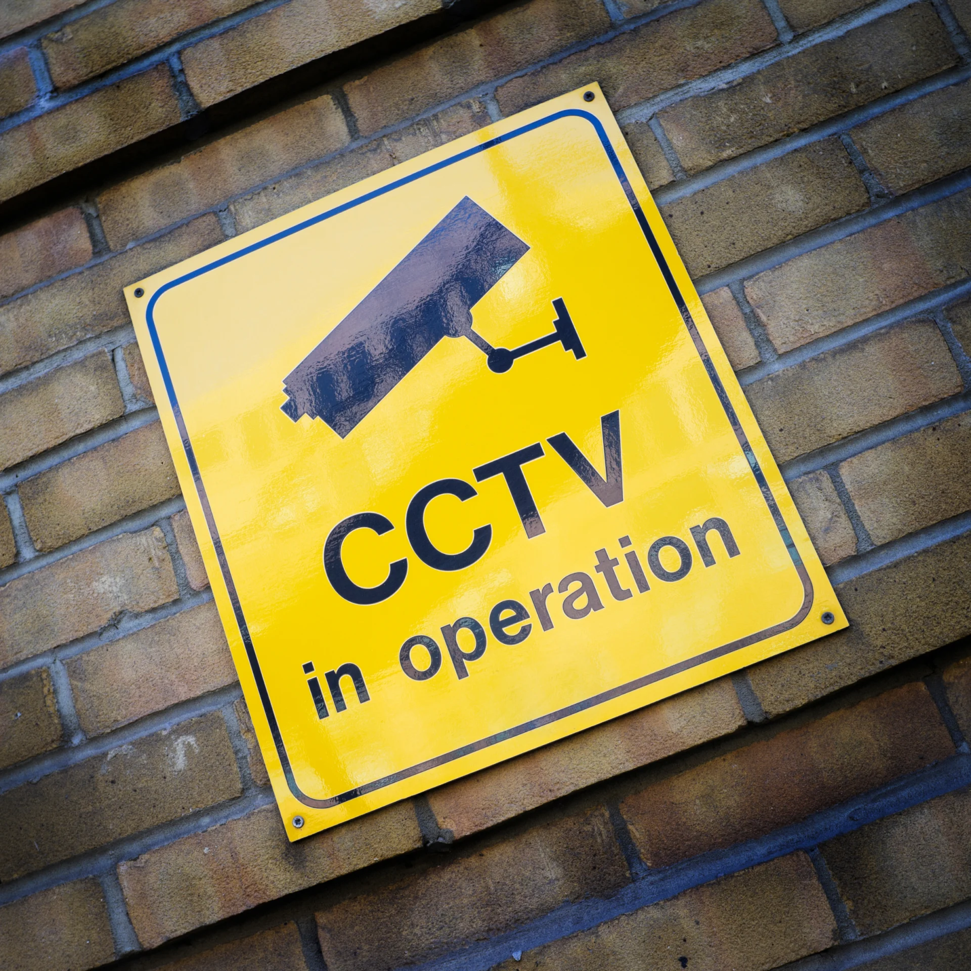 Yellow CCTV In Operation sign on a brick wall