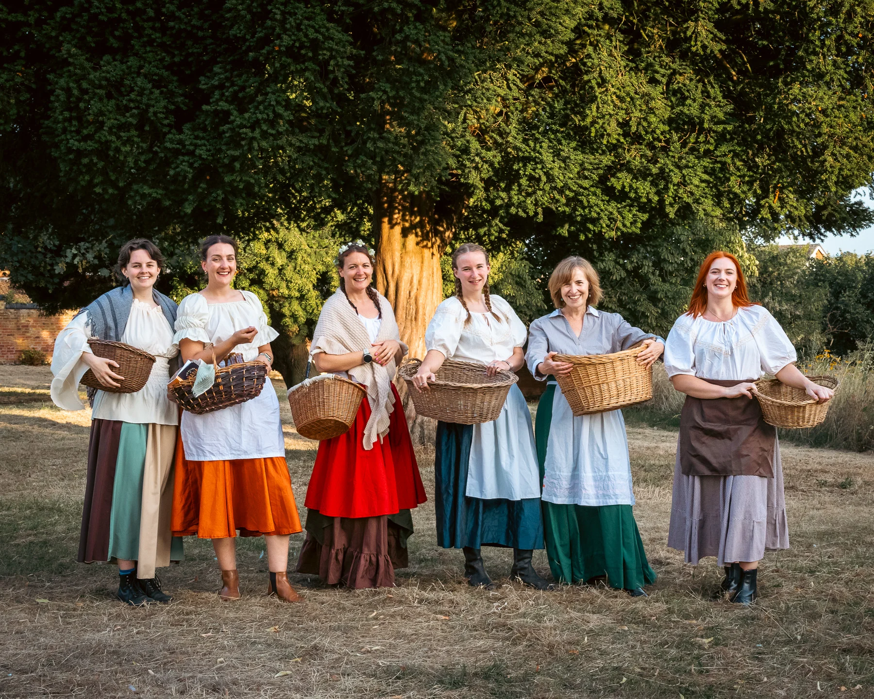 Six cast members of The Ballad of Maria Marten in period costume holding wicker baskets outdoors in Stone.