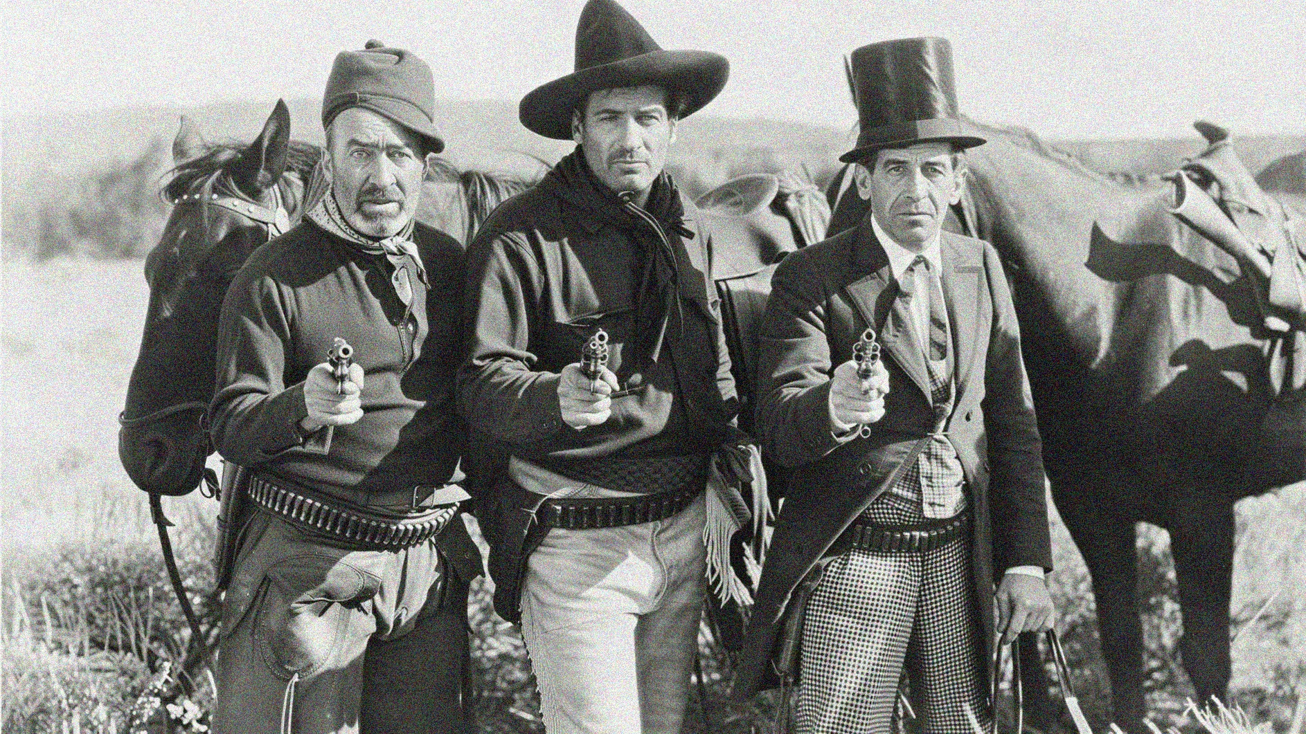 Black and white still from 3 Bad Men showing three armed men standing in front of horses.