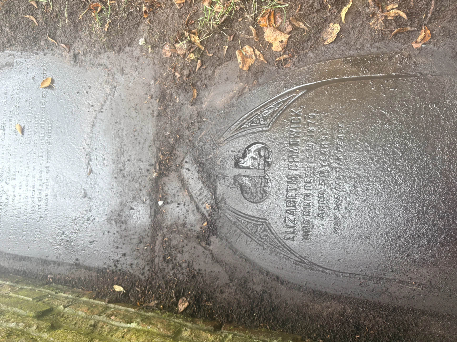 Partially uncovered flat headstones beside a stone wall in the churchyard at St Michael and St Wulfad’s Church in Stone.