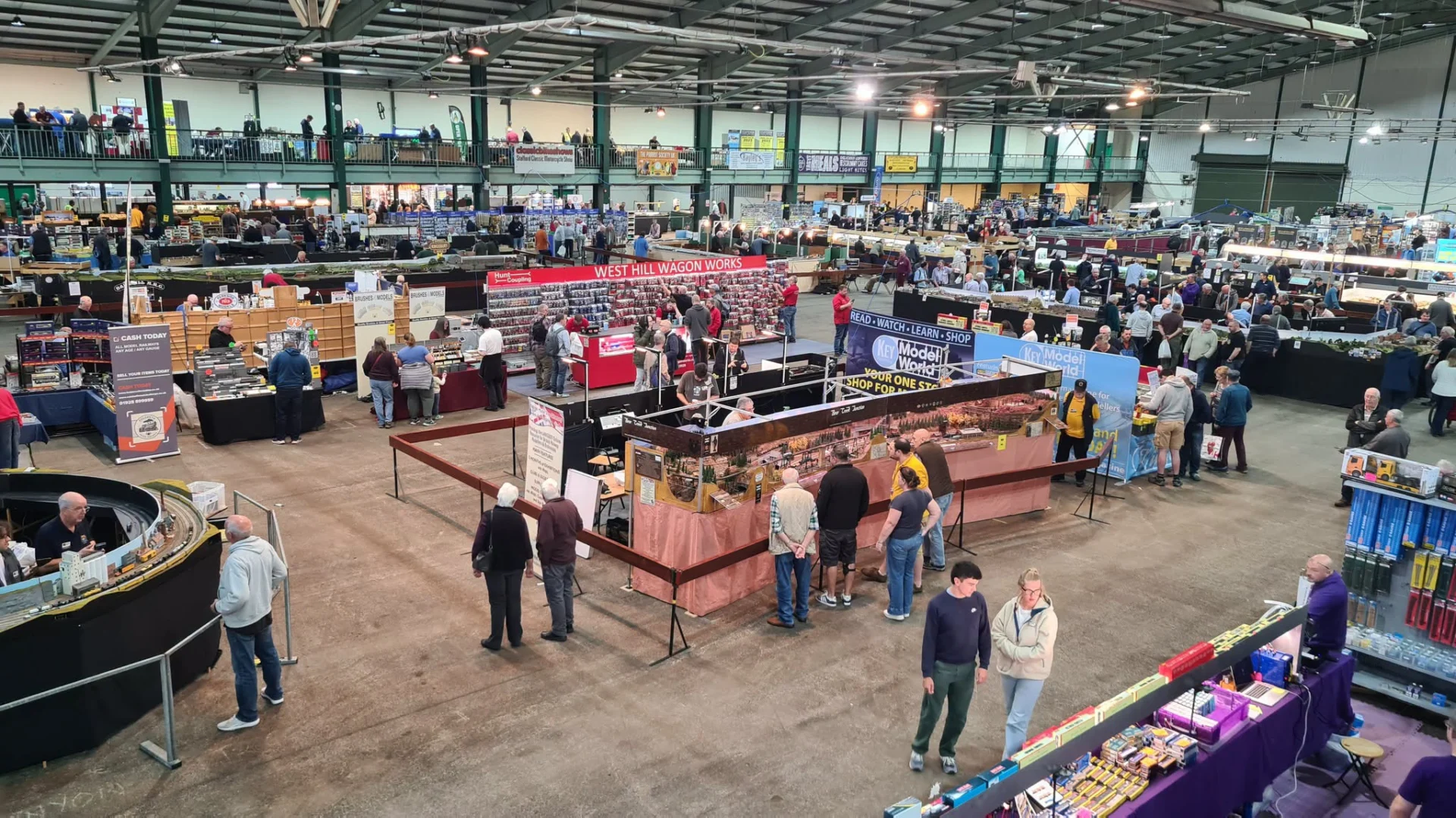 Visitors browsing model railway layouts and trade stands inside a large exhibition hall.