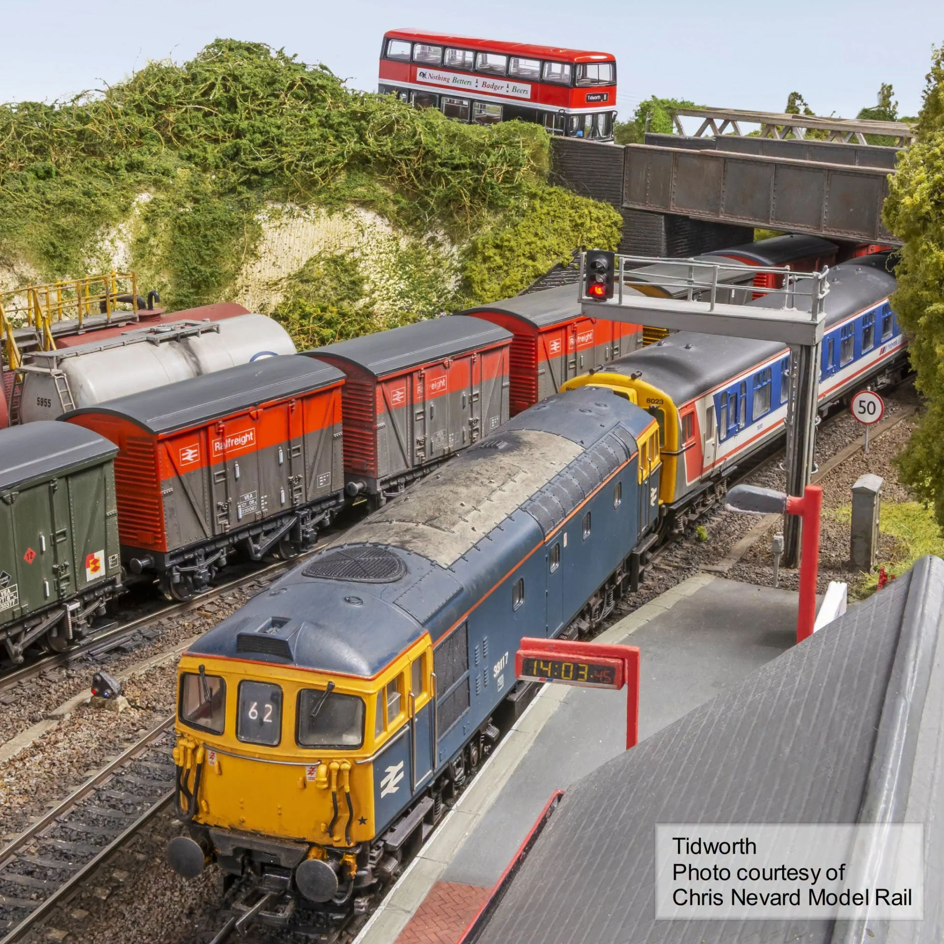 Blue and yellow model diesel locomotive alongside freight wagons and passenger coaches on the Tidworth model railway layout.