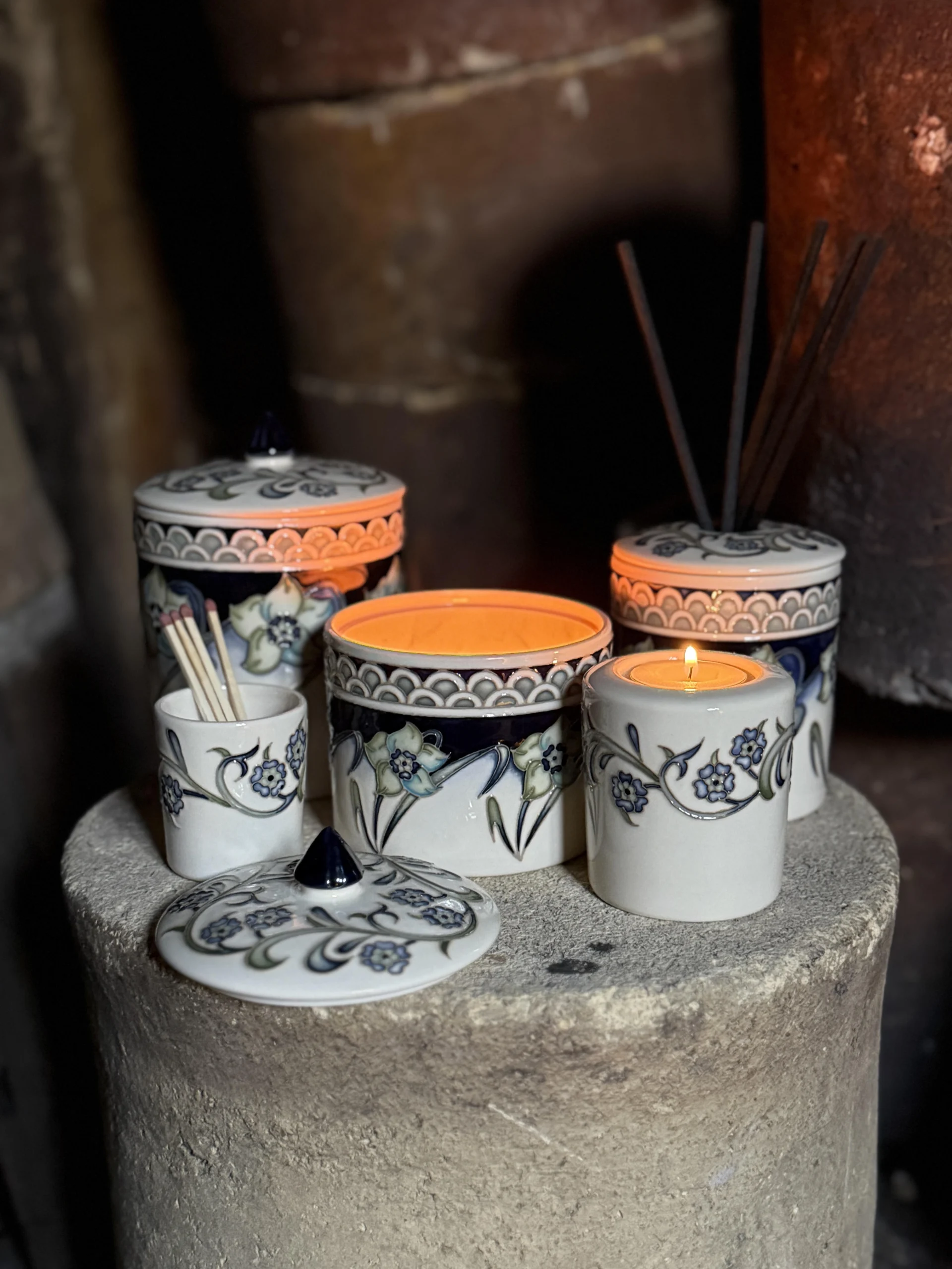 Moorcroft ceramic candle jars, diffuser, tea light and match pot from the collaboration with The Wandering Bee, arranged together with candles lit.