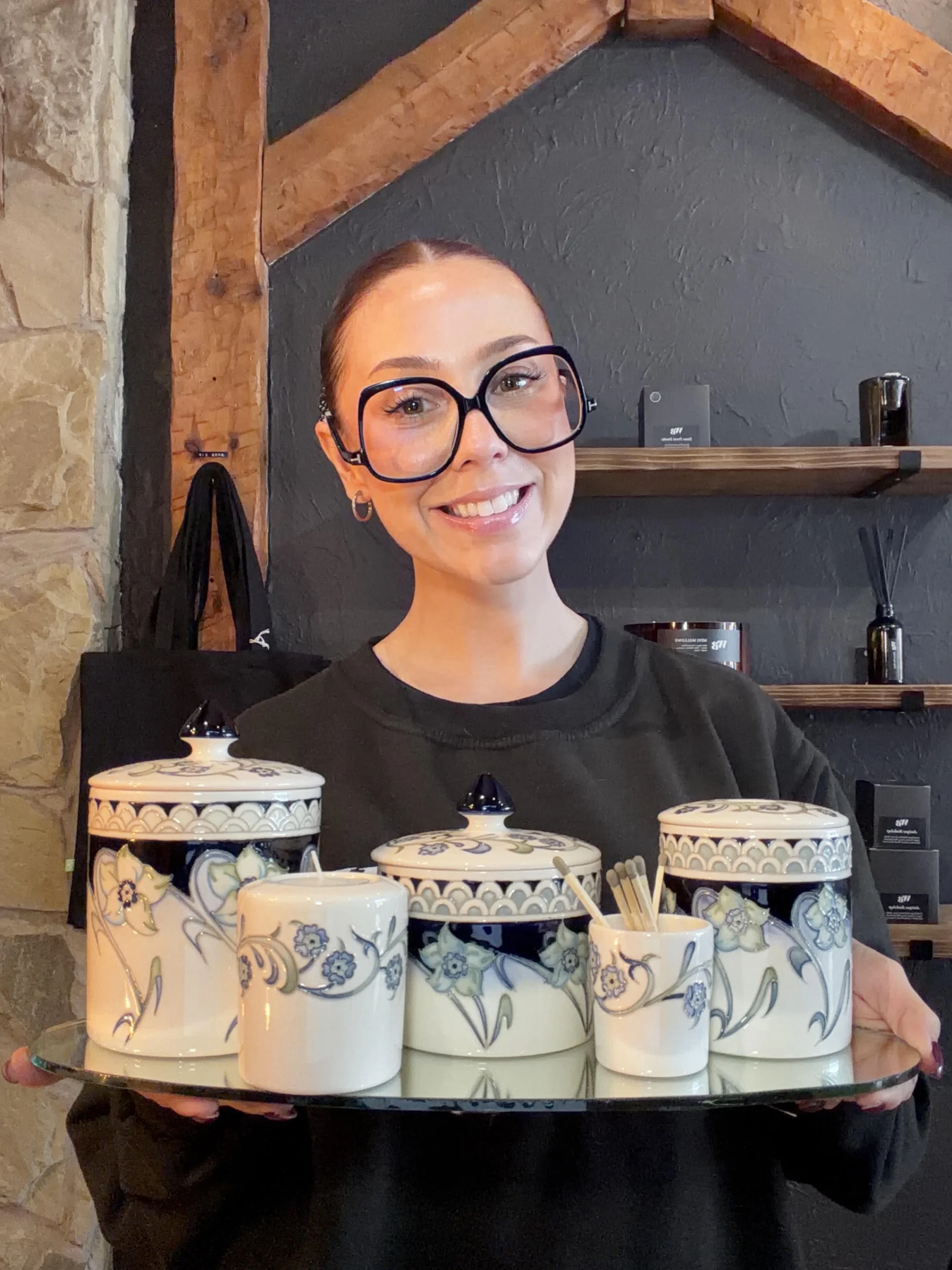 Beth Warren of The Wandering Bee holding a tray of Moorcroft ceramic candle and fragrance pieces inside the Stone shop.